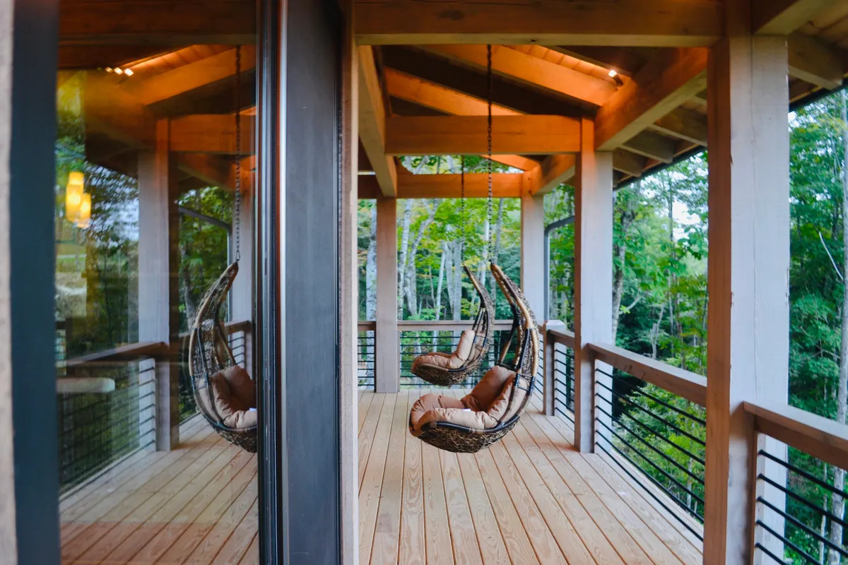 An inviting exterior space with hanging chairs, solid wooden beams, and surrounding greenery. The scene suggests relaxation, conversation, and enjoyment of nature, all set in a peaceful outdoor environment.