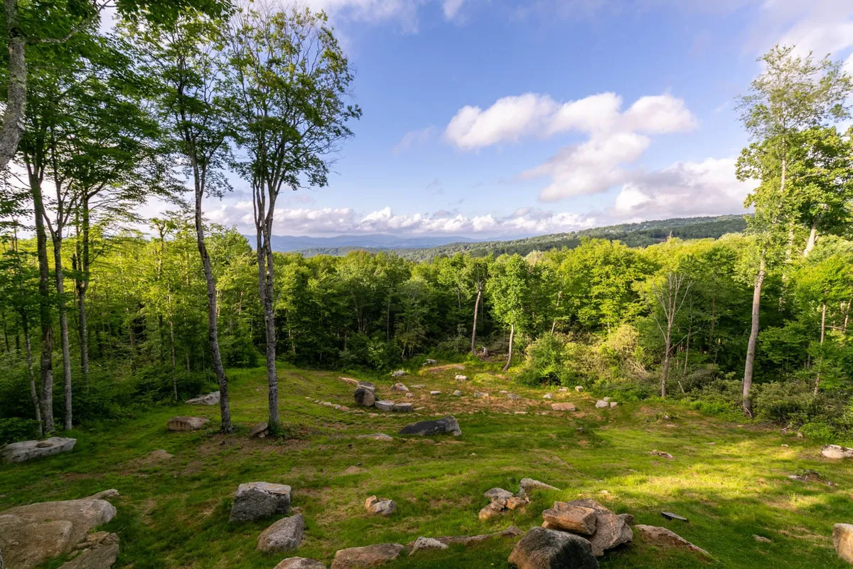 A scenic exterior shot of lush greenery, distant mountains, and scattered rocks, set in a peaceful natural environment. The landscape is tranquil, ideal for hiking, nature walks, and wildlife watching, with a hint of adventure and serenity.