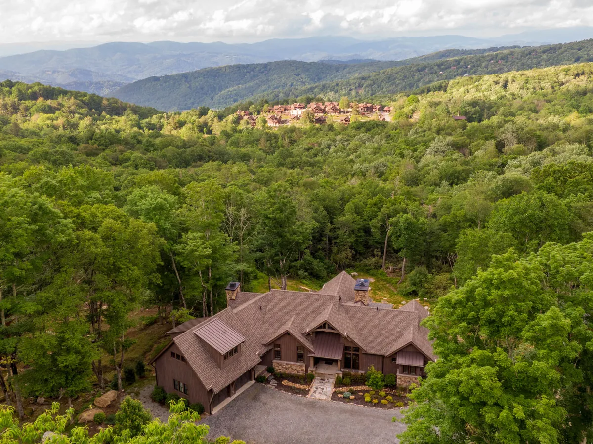 This image shows the exterior of Eagles Nest, framed by lush trees and a sweeping mountain range in the background. The house is nestled in nature, suggesting easy access to trails and vibrant outdoor scenery, with the porch inviting relaxation and seasonal observation.