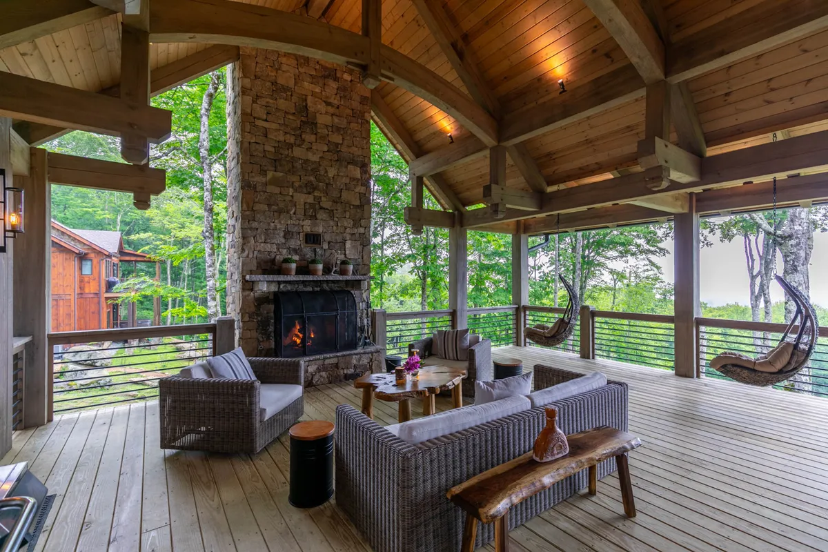 A tranquil outdoor scene featuring a covered deck area with a fireplace, comfortable seating, hanging chairs, and a stunning view of nature beyond. The space feels sheltered yet open, perfect for enjoying the outdoors in any season.