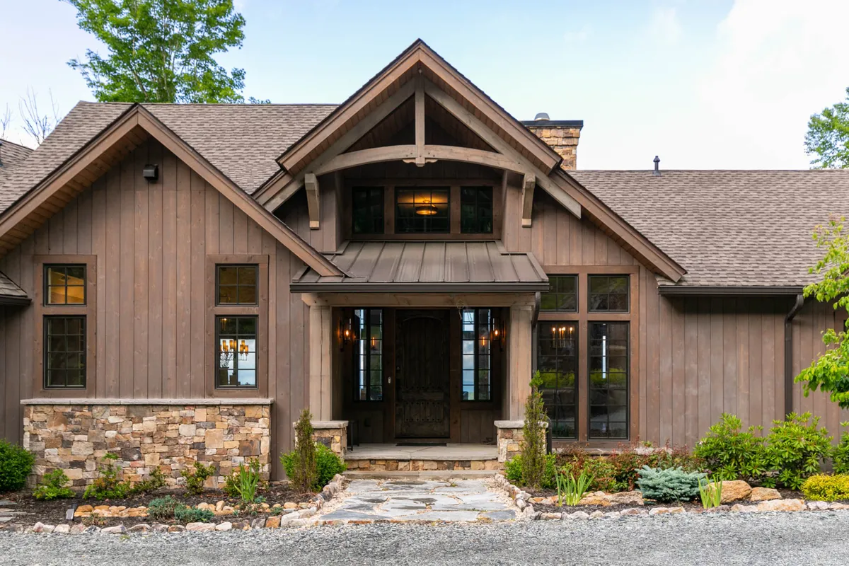 The scene highlights a beautiful wooden front door, a stone façade, and a landscaped garden, creating an inviting entryway. Friends are seen gathering, enjoying the outdoors and the comfort of the home’s entrance.
