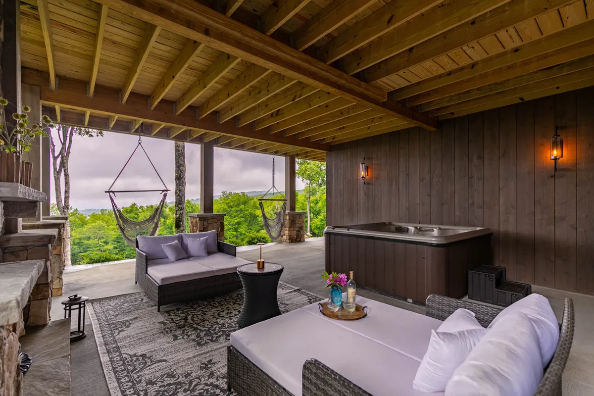 An inviting exterior shot of a deck with hammocks, a hot tub, and ample seating set among verdant plants. The vantage point showcases the interconnectedness of the outdoor spaces, with multiple areas for lounging and socializing while enjoying views of the surrounding landscape.