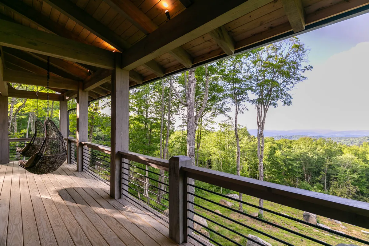 A wooden deck with a hanging chair overlooks a sweeping landscape, with supporting beams and the scenic view beyond providing a peaceful, private outdoor setting.